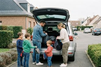 Famille nombreuse chargeant bagages dans le coffre d'un grand monospace 7 places dans une allée résidentielle